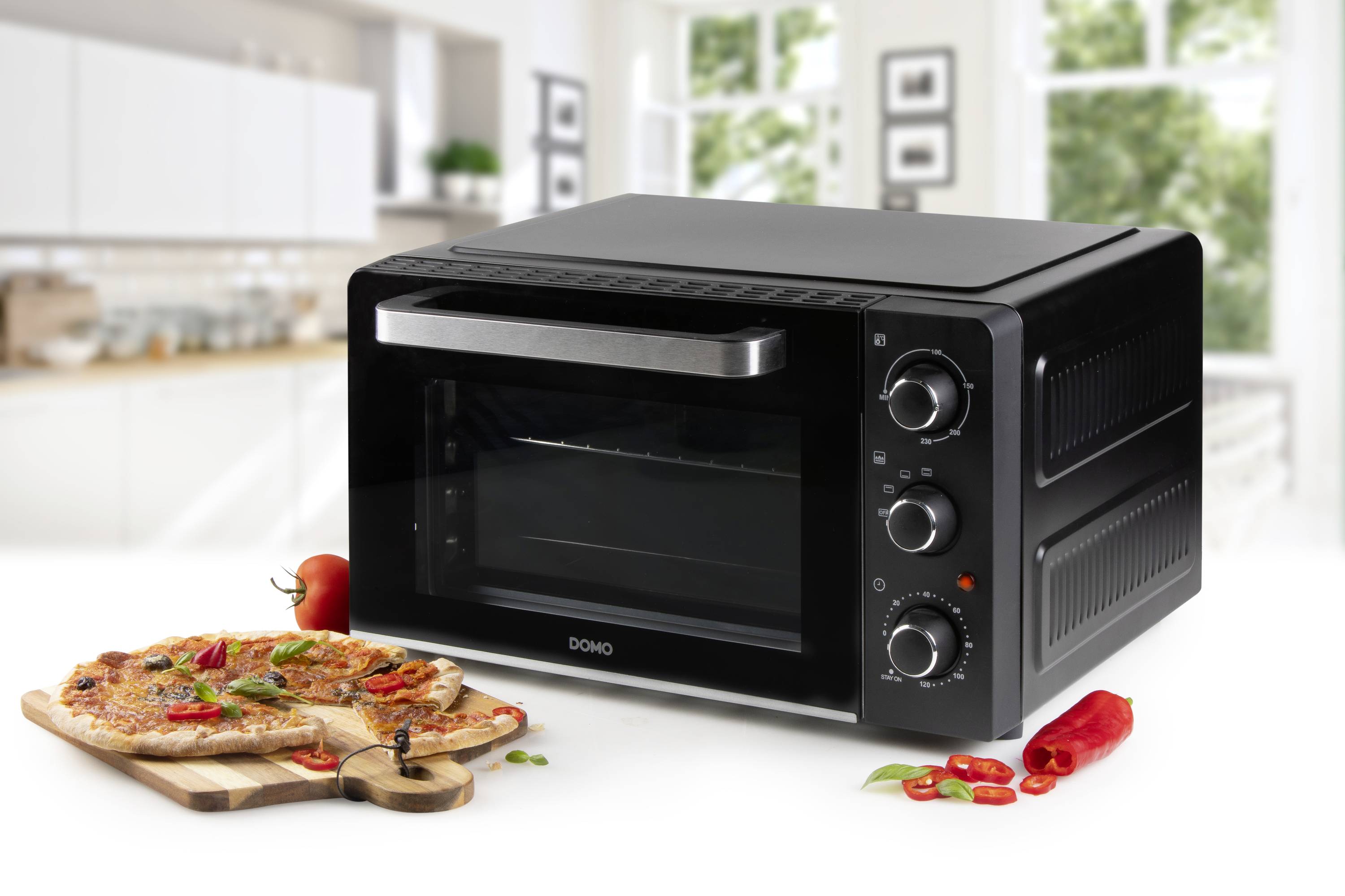 Kompaktní černá mini trouba v moderní kuchyni, vedle níž je pizza na dřevěné desce.