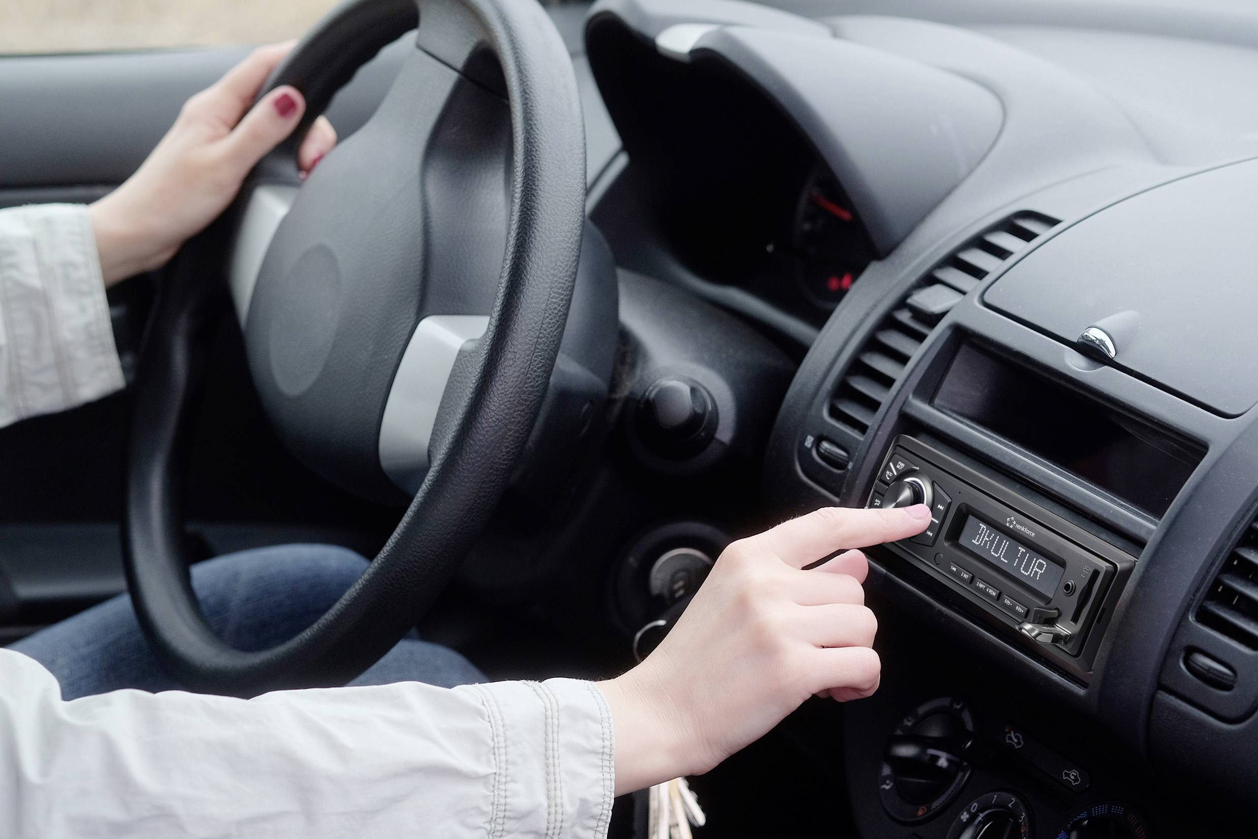 Řidič otáčí knoflíkem autoradia, přičemž druhou rukou drží volant. Nastavení zvuku v automobilu.