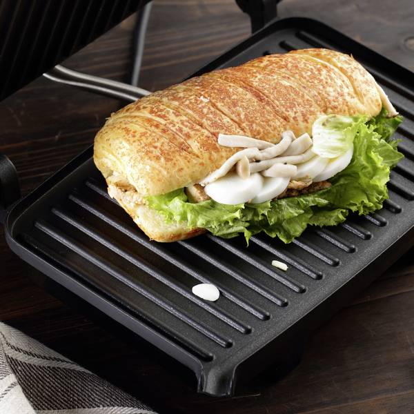 Křupavá, grilovaná sendvič s kuřecím masem, salátem a cibulí leží na stolním grilu.