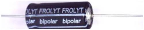 Kondenzátor s nápisem 'bipolární' a 'Frolyt', černý válcovitý tvar se dvěma drátovými vývody.