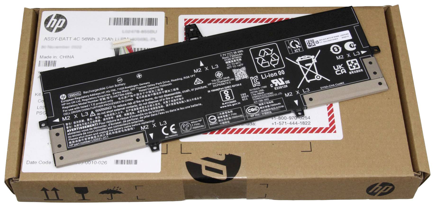Baterie notebooku leží na kartonu s logem HP. Baterie je černá s bílými bezpečnostními a ověřovacími štítky a technickými specifikacemi.