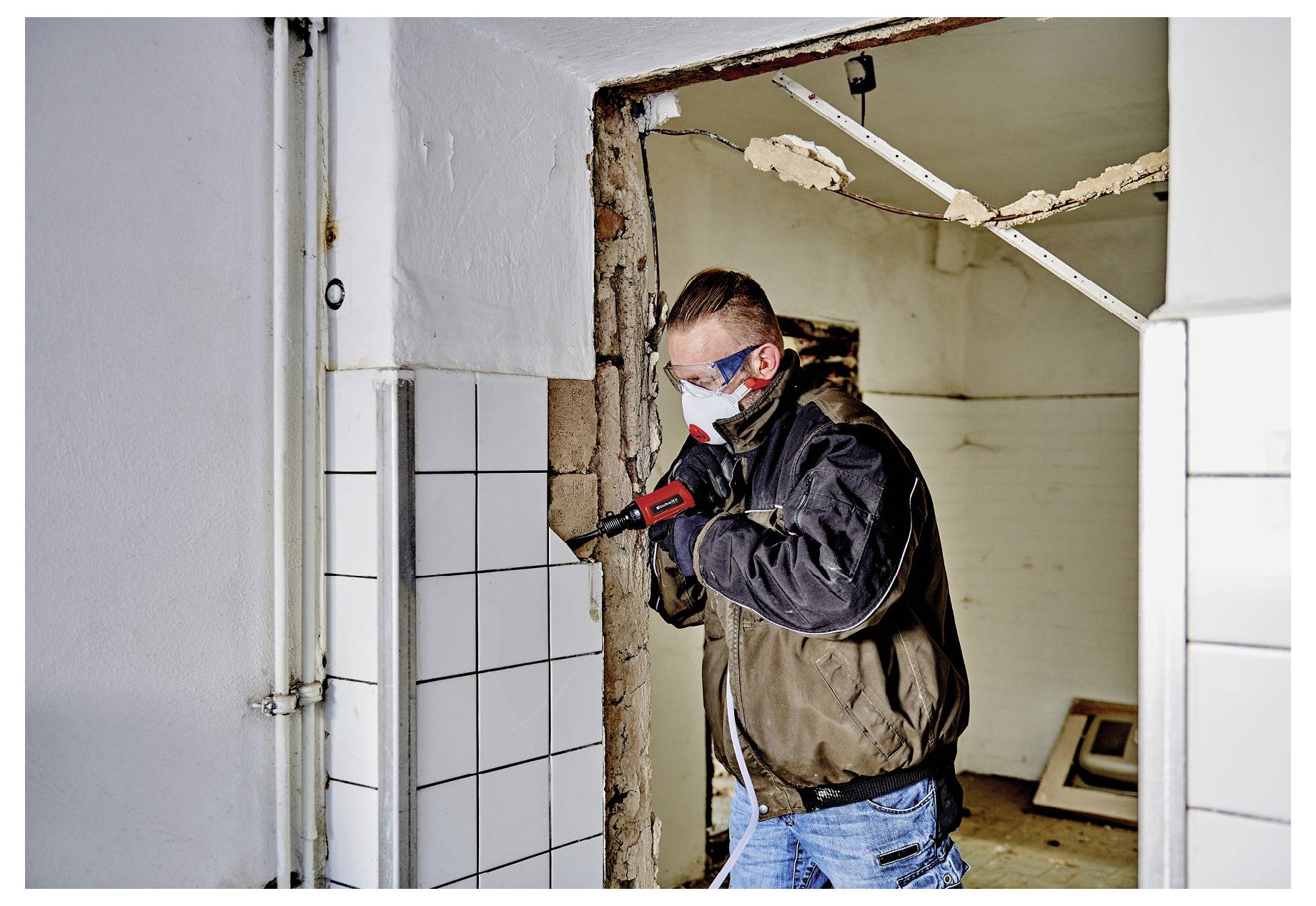 Stavbyvedoucí používající vrtací kladivo k odstranění obkladů kolem dveří během vnitřní demolice nebo renovace.
