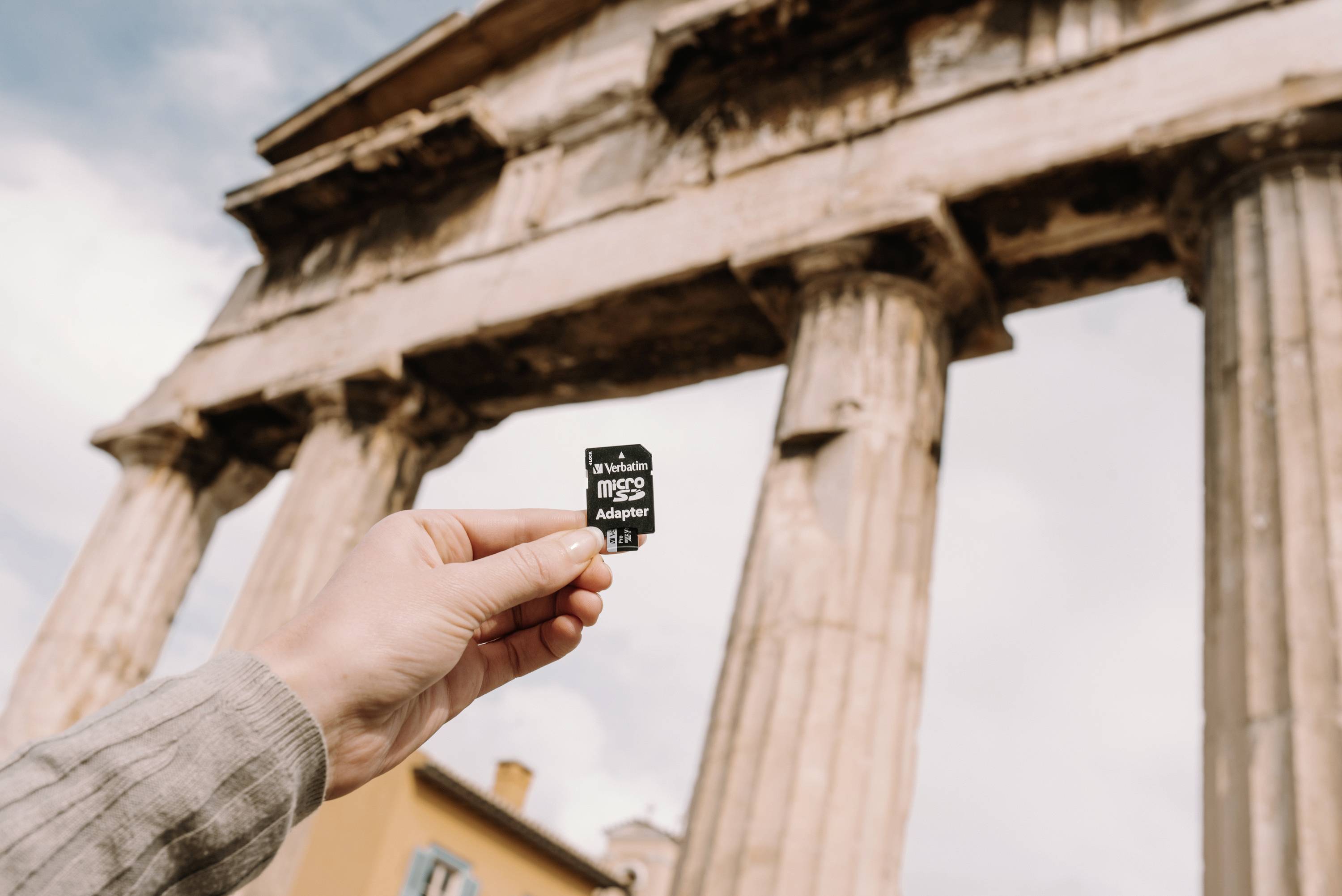 Jedna ruka drží 4GB microSD kartu před antickým řeckým chrámem s sloupy. Obloha je lehce zatažená.