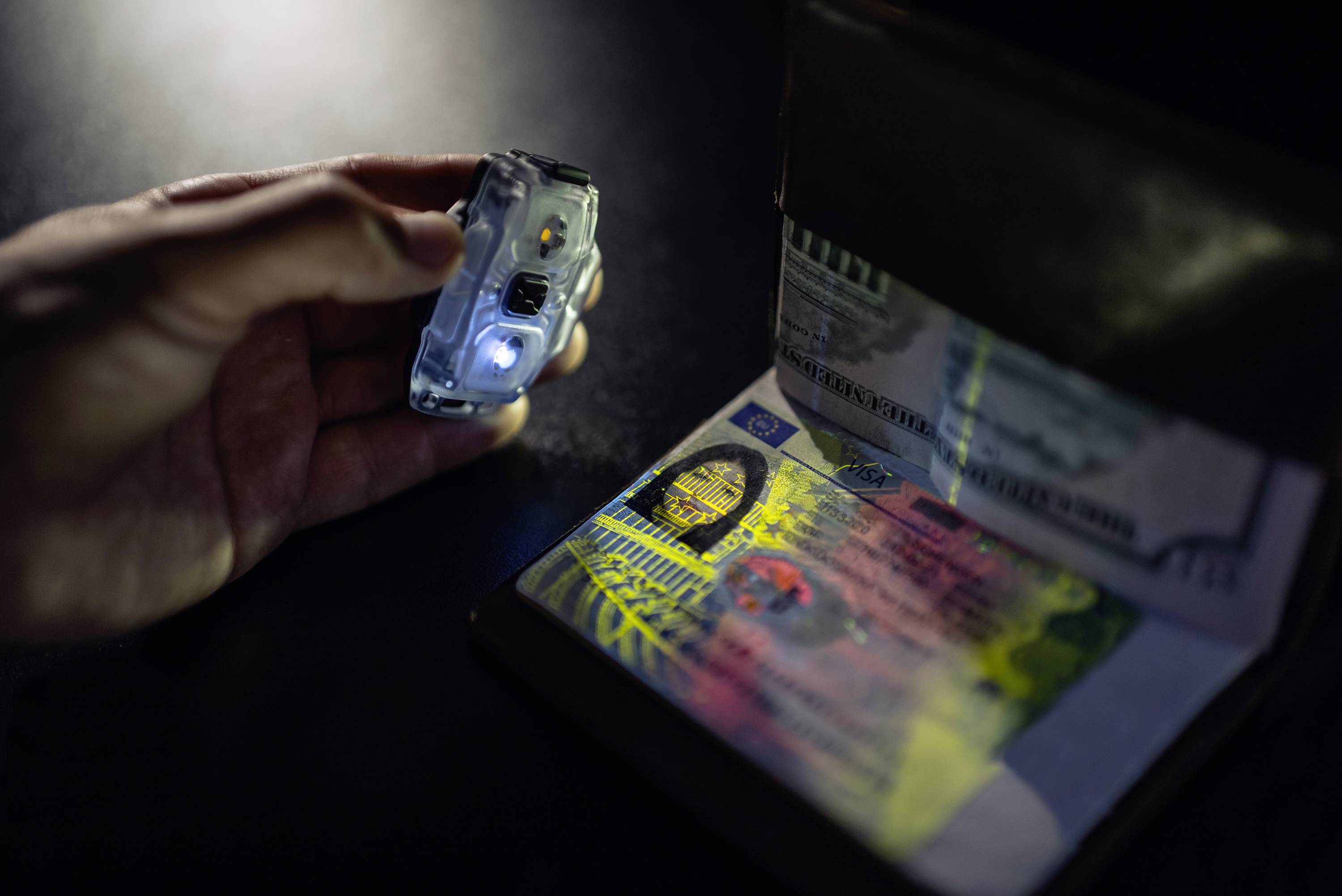 Osoba kontroluje identifikační doklad pomocí ultrafialového světla, aby odhalila bezpečnostní prvky.