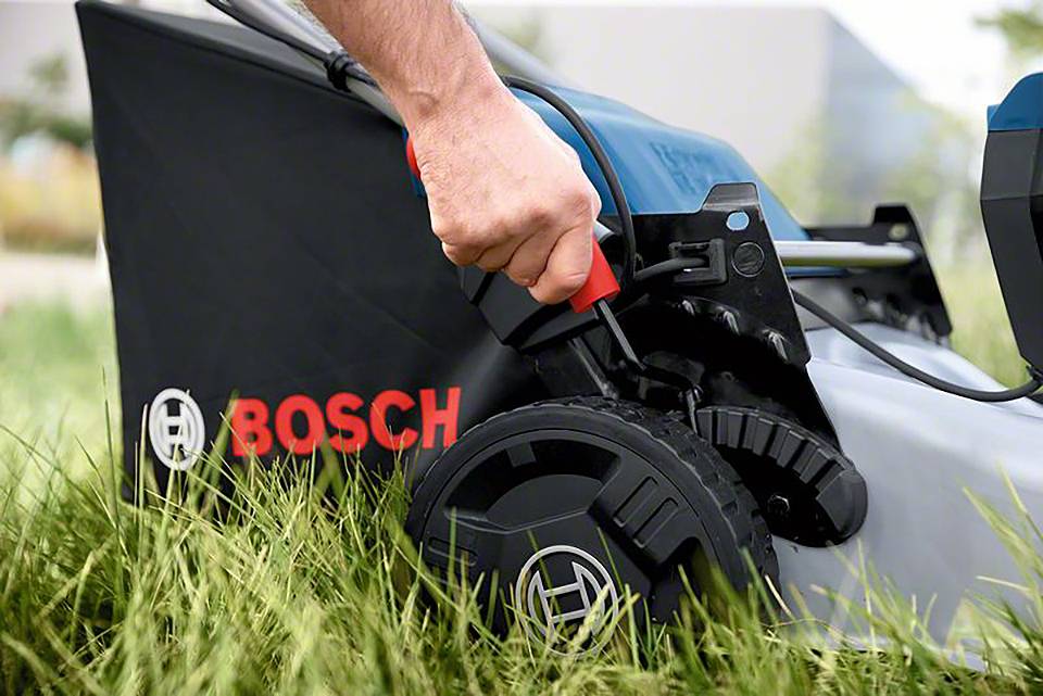 Člověk nastavuje výšku sečení u sekačky Bosch pomocí kola ve vysoké trávě.