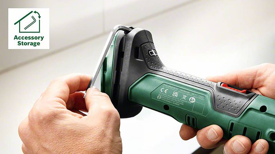 Osoba drží zelený elektrický nástroj, pravděpodobně úhlovou brusku. V levém horním rohu symbol 'Uložení příslušenství'.