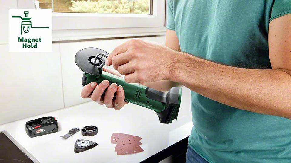 Muž vymění díl zařízení na elektrickém nástroji pomocí magnetického držáku nástrojů. Vedlejší díly leží vedle něj.