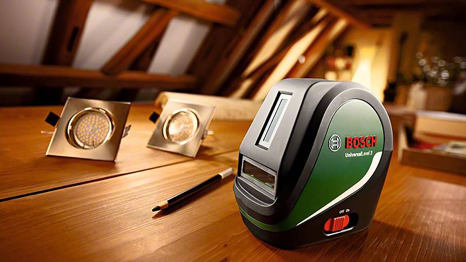 Elektronické zařízení od Bosche na dřevěném stole se dvěma LED diodami a tužkou. Typické prostředí denní dílny.