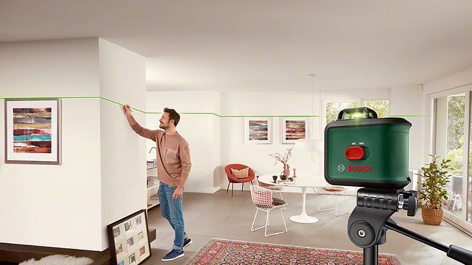 Muž používá laserový přístroj Bosch k vedení přímé čáry na stěně v moderním obývacím pokoji.