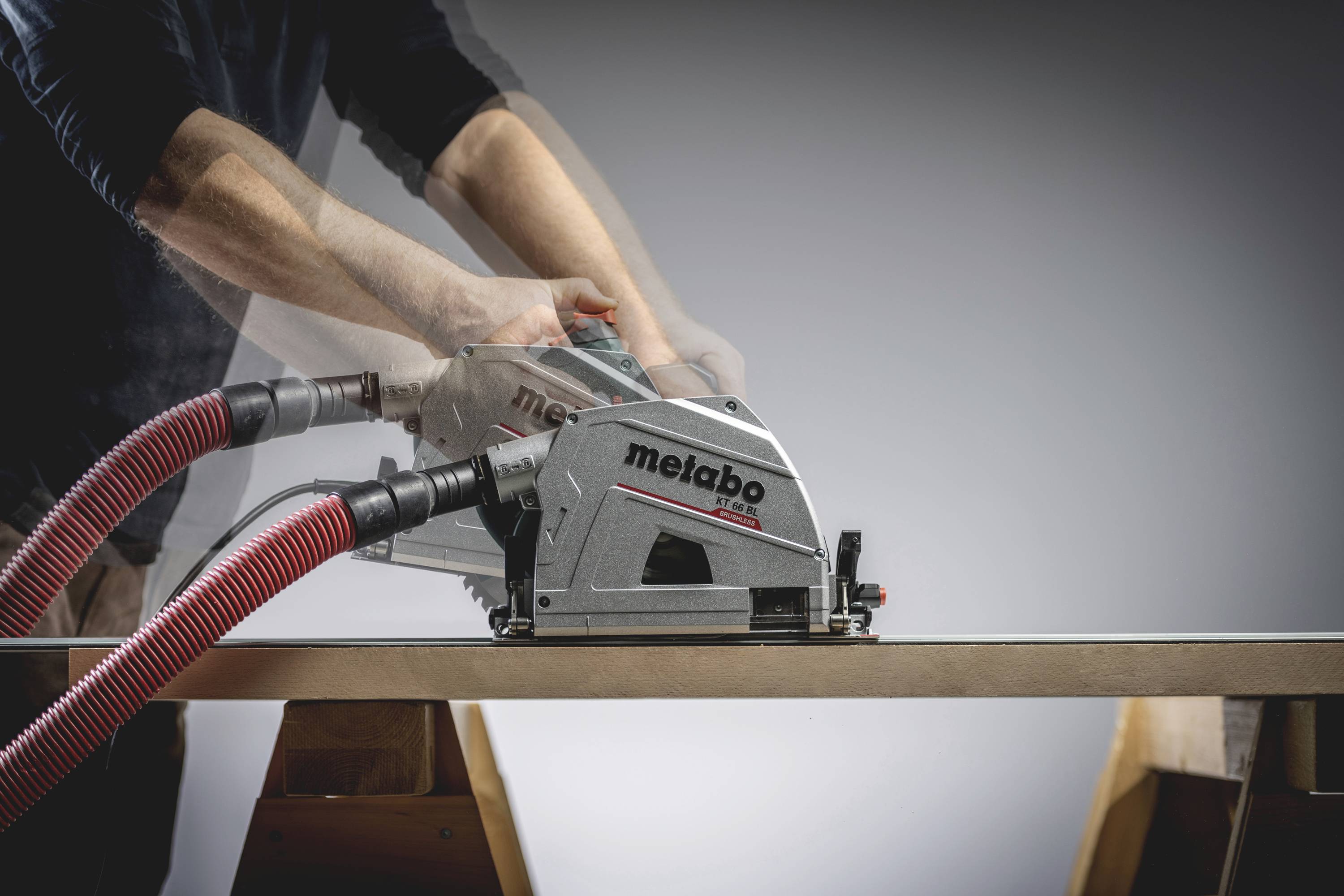 Osoba řeže dřevěnou desku kotoučovou pilou Metabo na řezacím stojanu, připojen je červený hadice, je viditelné rozmazání pohybu.