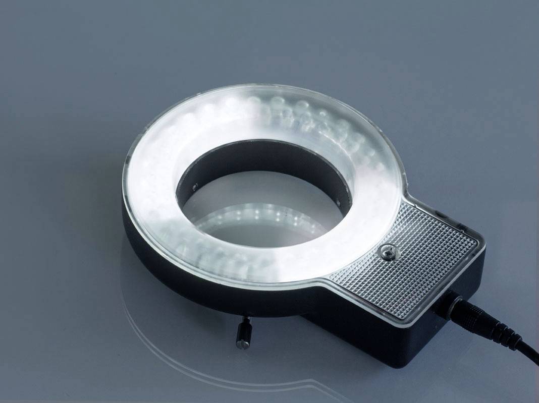 Kulatý LED kroužek s černým pouzdrem a svítícími bílými LED diodami, ležící na reflexní ploše.