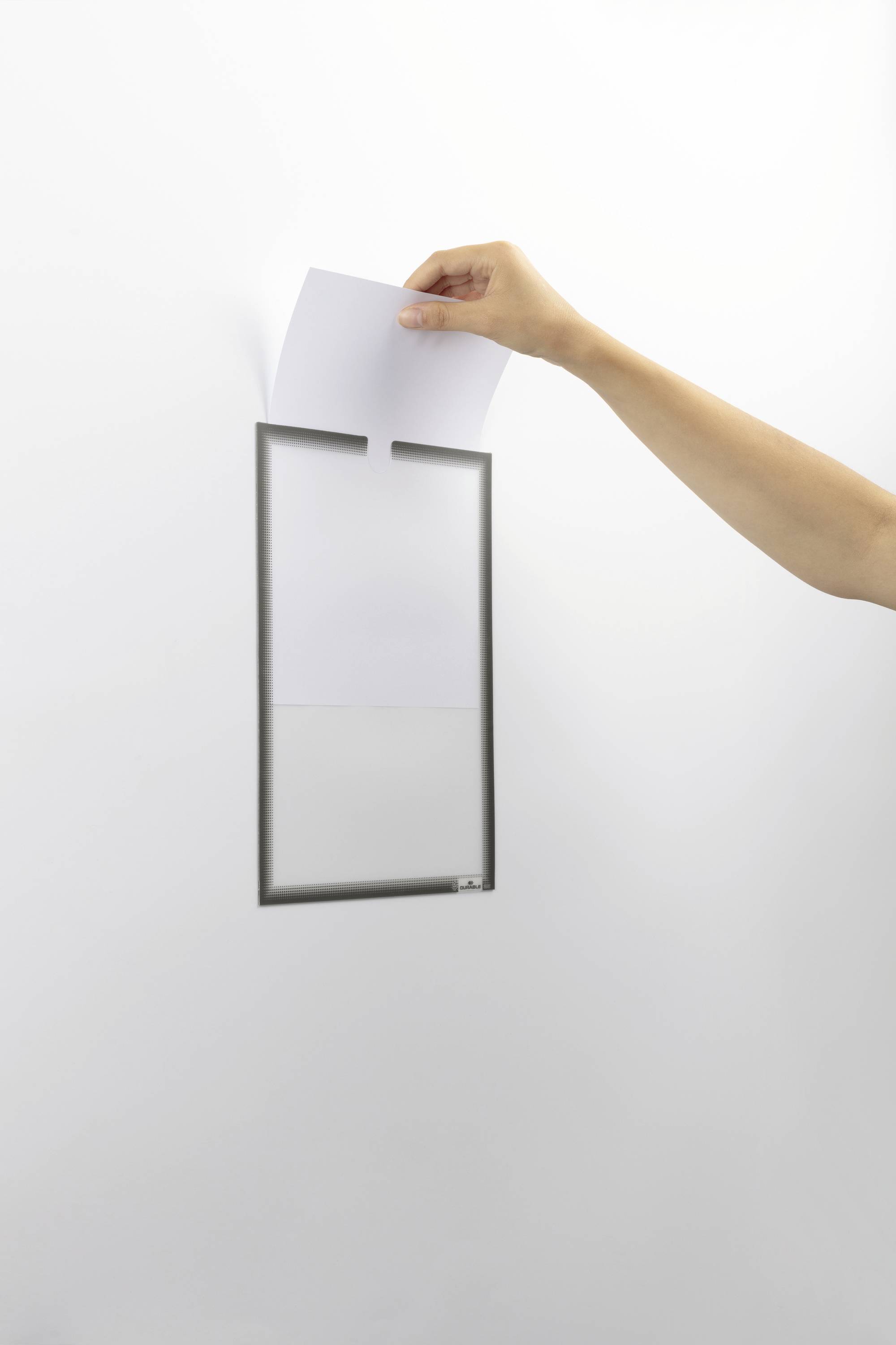 Ruka vhazuje list papíru do poštovní schránky. Důraz je kladen na samotný akt vhazování.