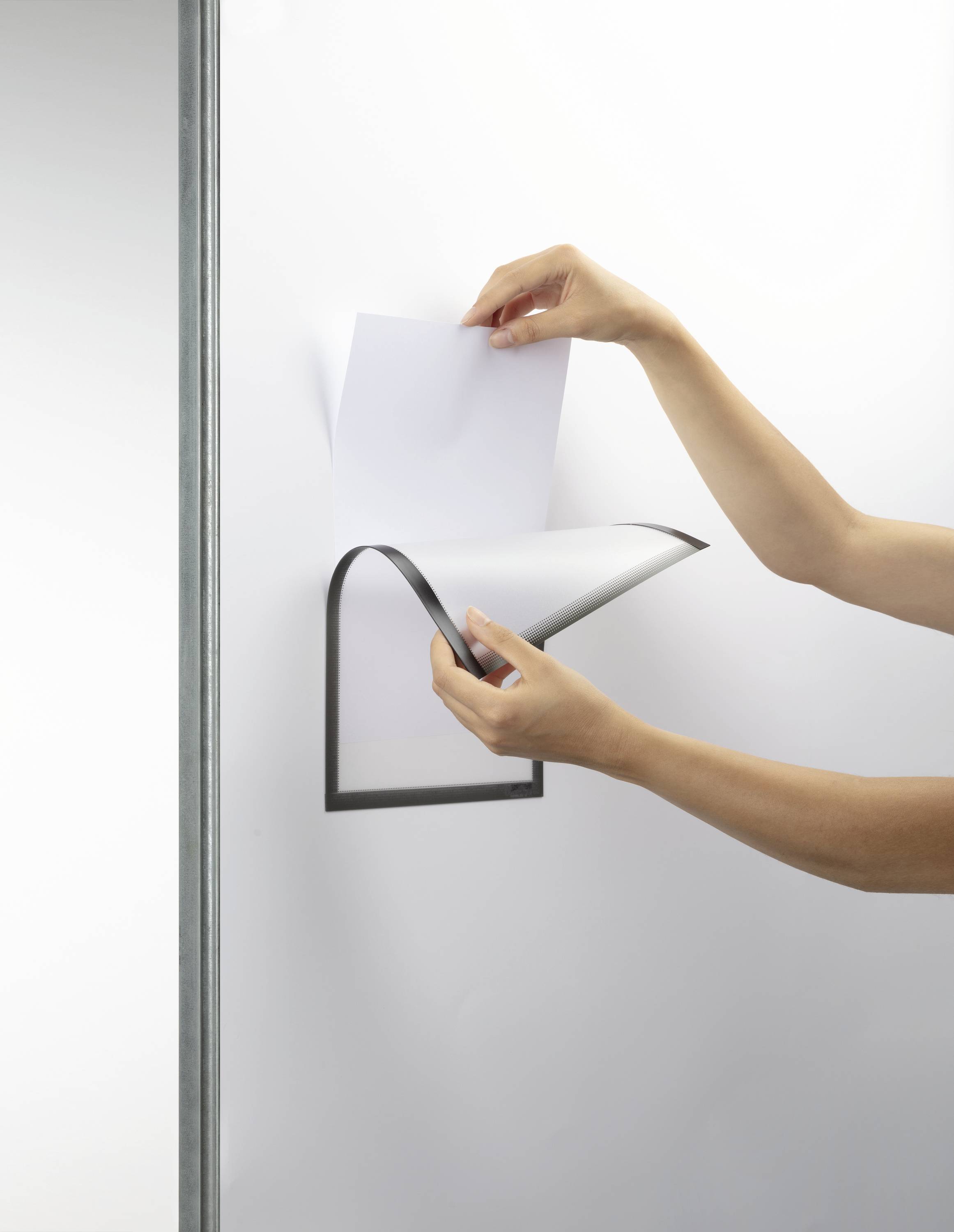 Osoba listuje papírovým držákem na zdi. Držák má minimalistický, moderní design v černé barvě.