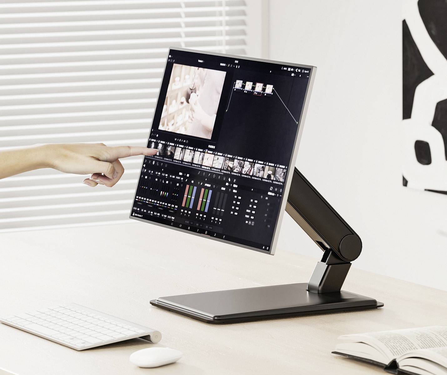 Ruka ukazuje na monitor s videoredakčním softwarem na pracovním stole. V pozadí jsou viditelné žaluzie.