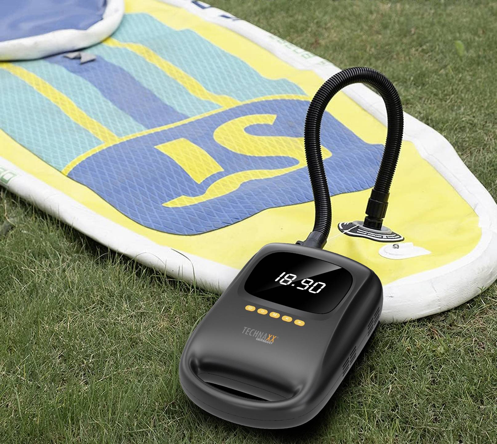 Nafukovací pumpa na trávě vedle nafukovacího paddleboardu s modrými a žlutými pruhy, připravená k napumpování.