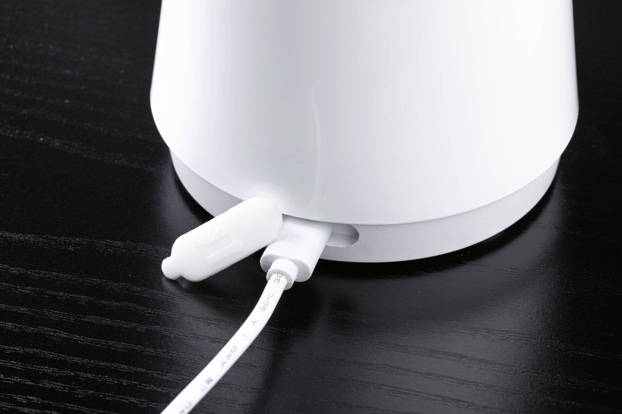 Bílý kabel je připojen na spodní straně bílého zařízení, které stojí na černém stole.