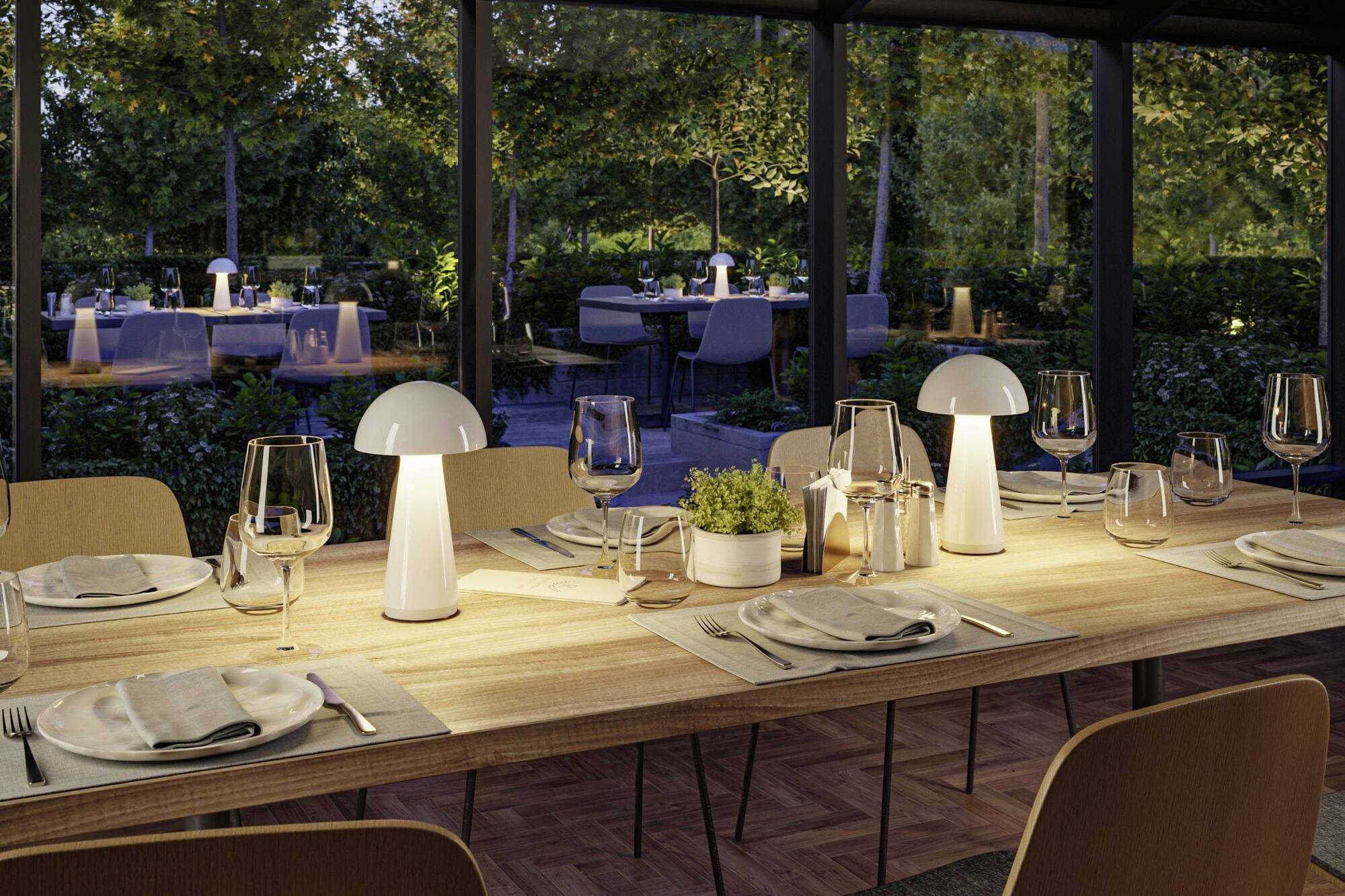 Elegantně prostřený jídelní stůl venku s moderními lampami a sklenicemi na víno, obklopený stromy, vytváří příjemnou atmosféru.