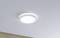 Kulatá, bílá stropní lampa svítí na světlém stropě. Prostředí je minimalistické.