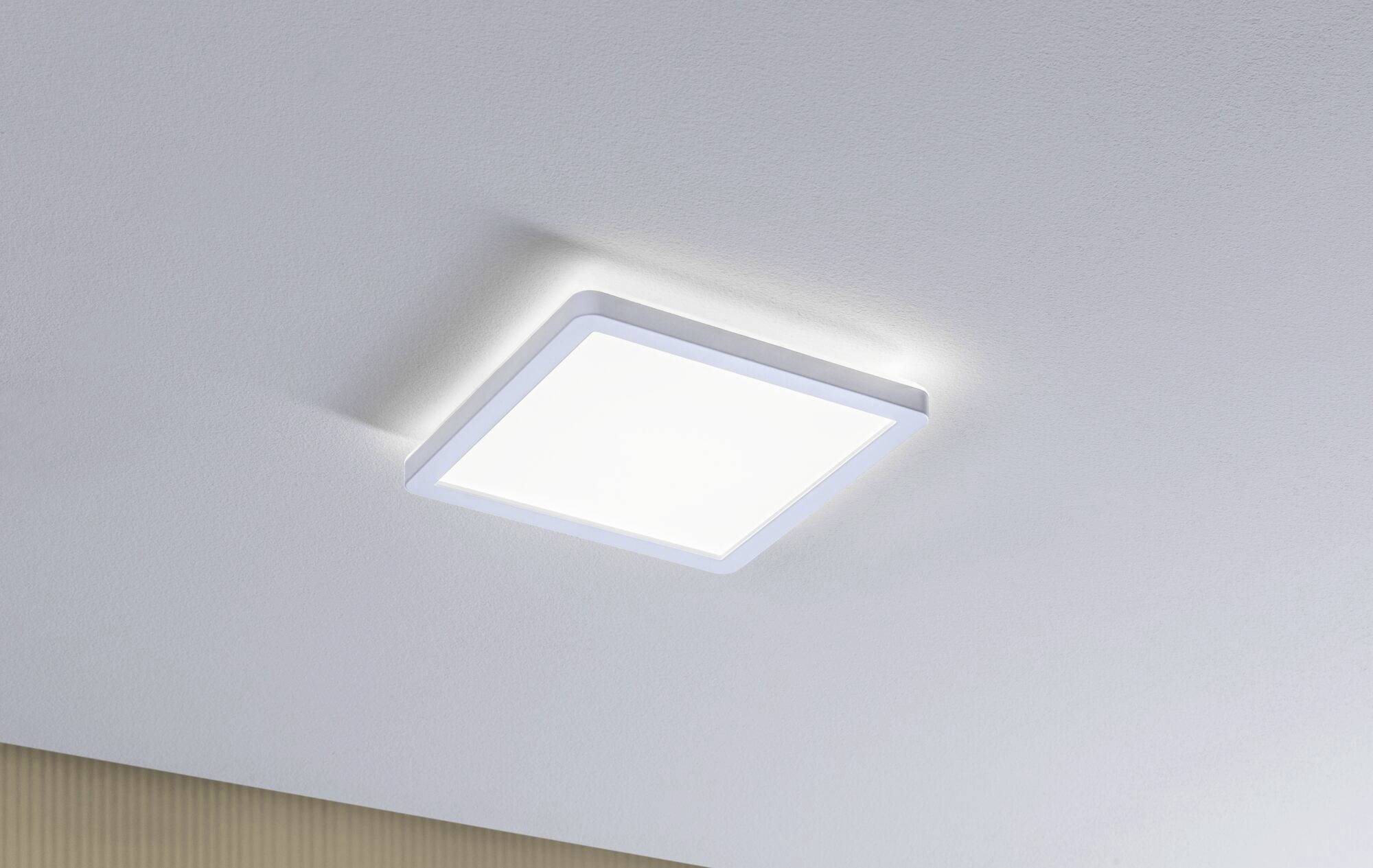 Čtvercové LED stropní svítidlo s bílým rámečkem svítí v místnosti s bílým stropem.