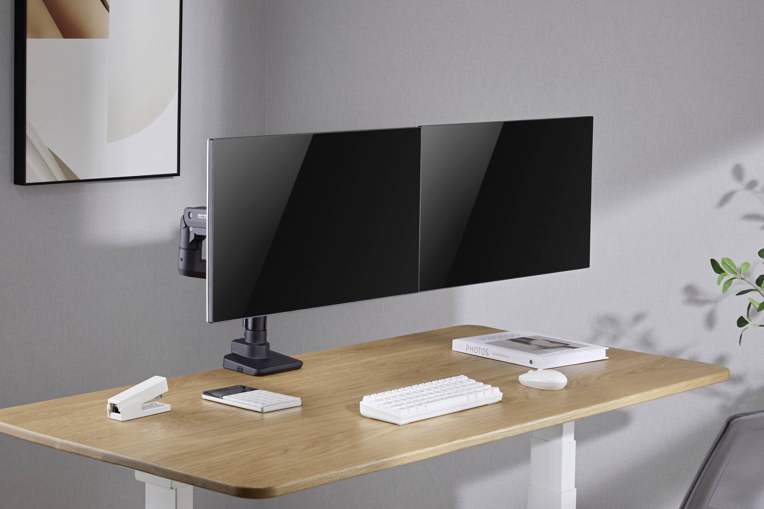 Dva velké monitory na moderním psacím stole; vedle nich klávesnice, myš, smartphone, kniha a poznámkový blok.