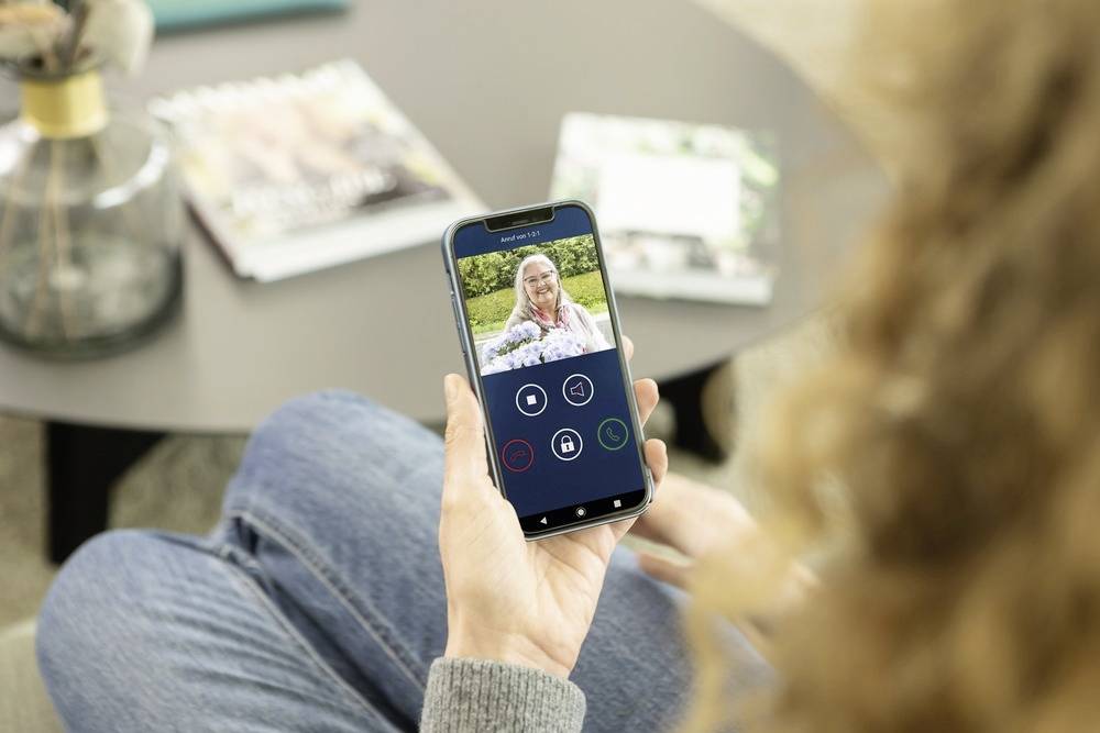 Jedna osoba provádí videohovor na chytrém telefonu. Na obrazovce je vidět člověk sedící v zahradě.