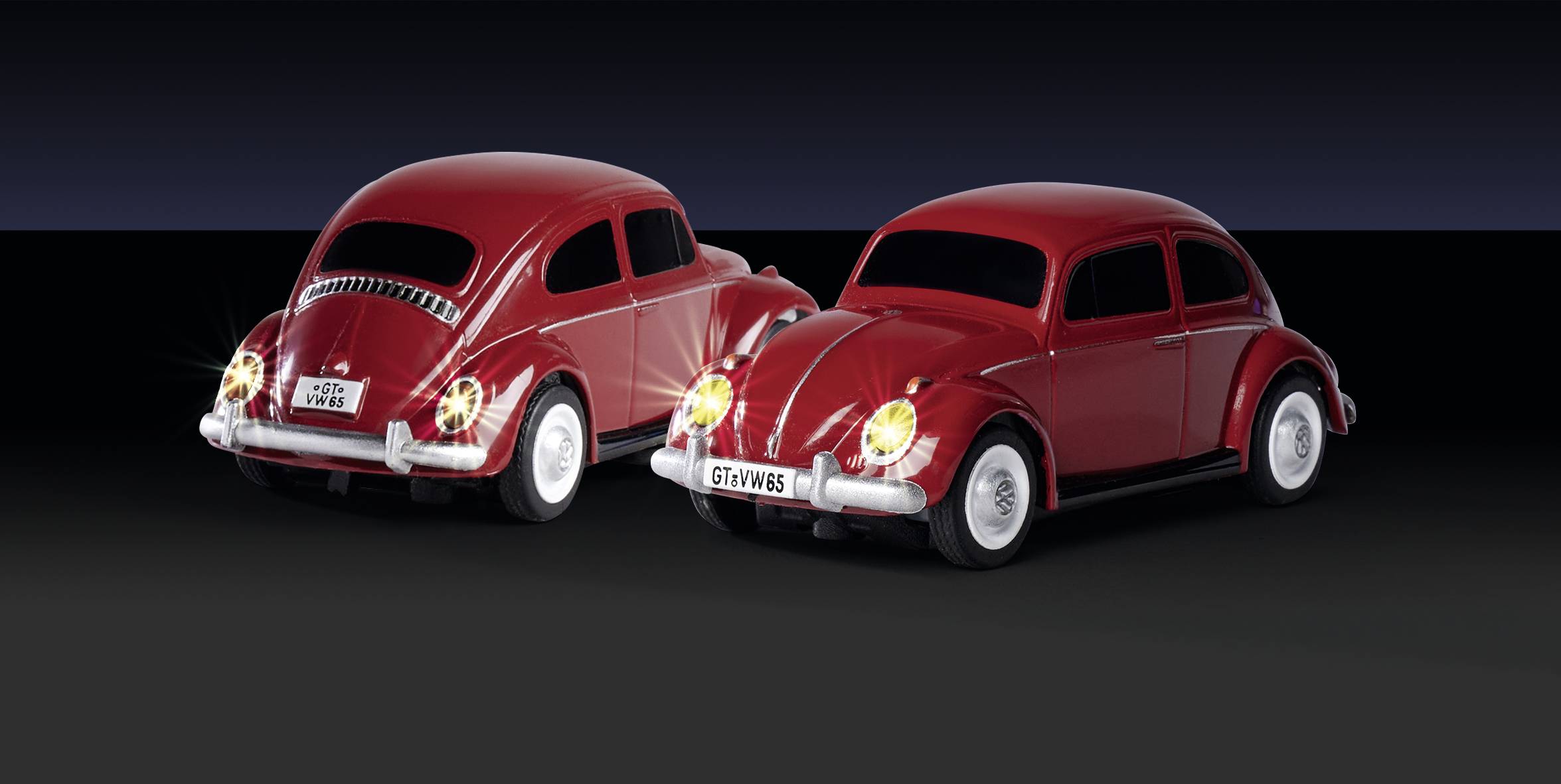 Dva červené modely klasického VW Brouka stojí vedle sebe na černém pozadí.