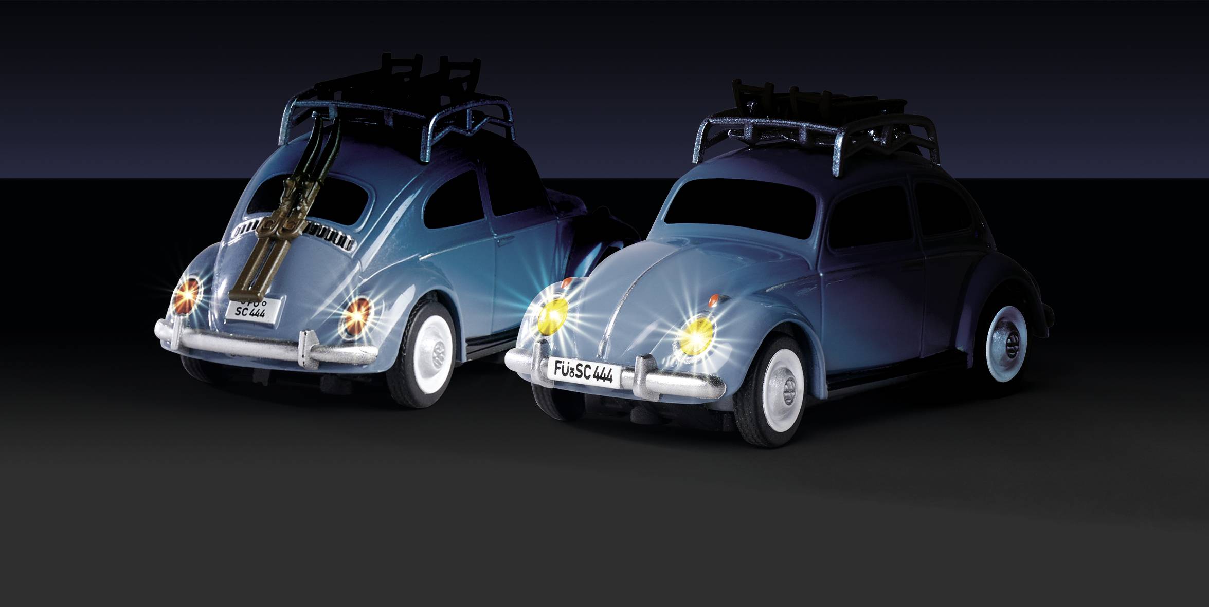 Dva nostalgické automobily s příčníky na střeše v tmavém prostředí, oba viditelné zezadu. Jeden automobil svítí světlomety.