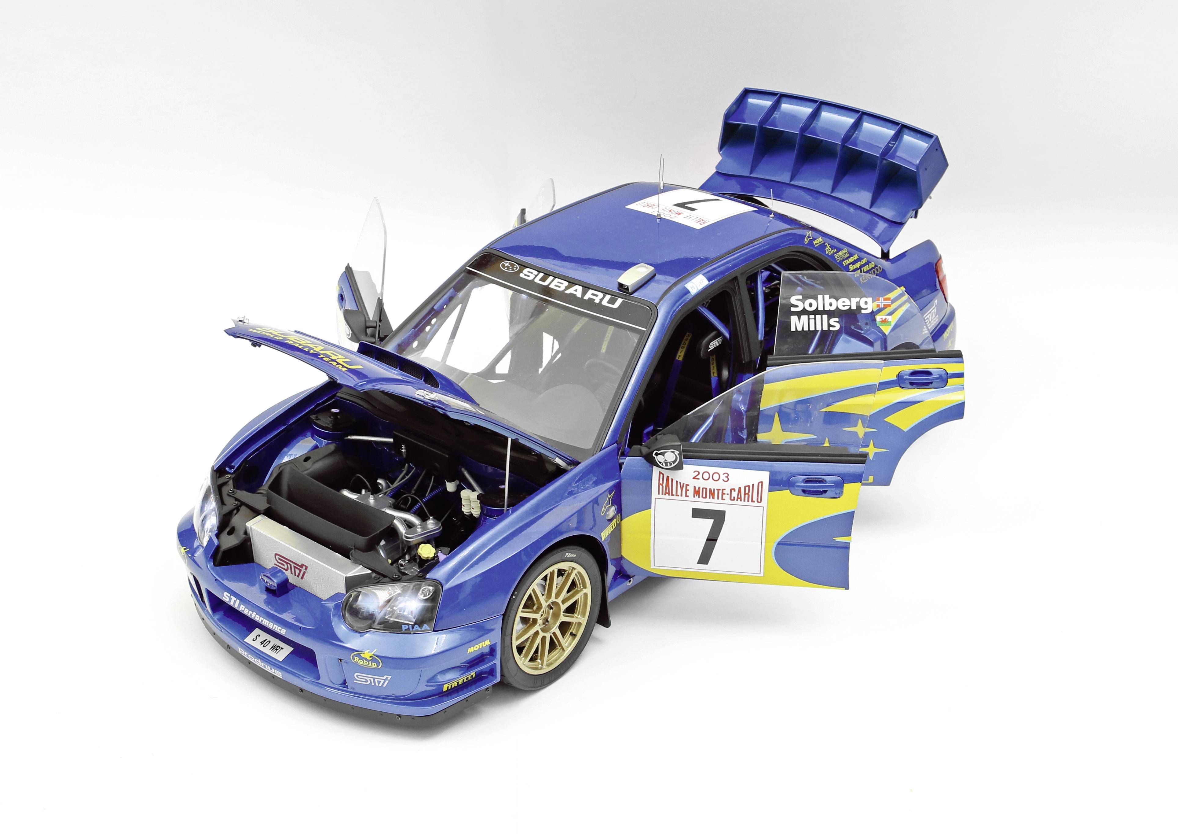 Modré modelové auto s otevřenými dveřmi a kapotou. Auto nese číslo 7 a má rallye samolepky.
