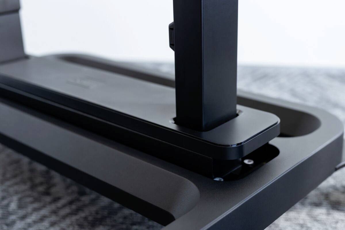 Detailní záběr černého, moderního stolního držáku na monitory. Držák je stabilně upevněn na šedém stole.