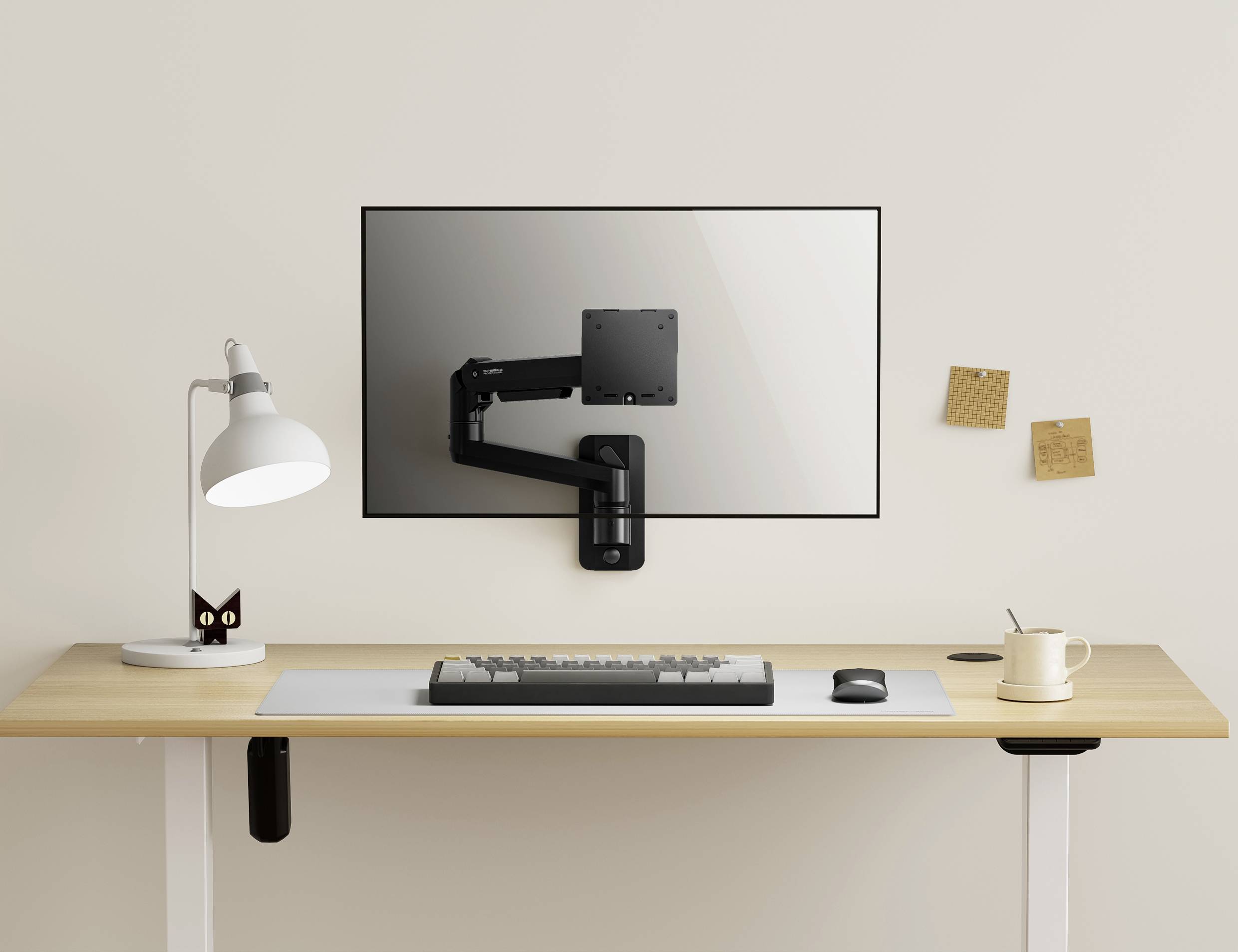 Minimalistický psací stůl s lampou, bílou podložkou pod myš, šálkem a klávesnicí. Na stěně je připevněná ramena monitoru bez monitoru.