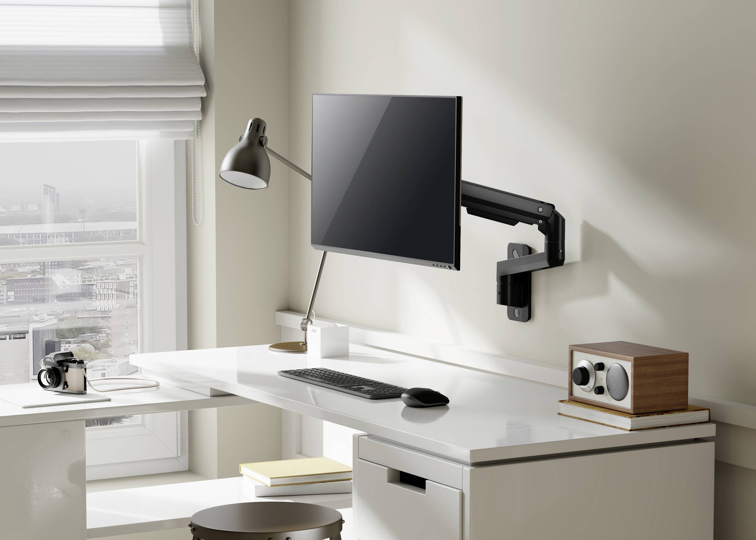 Moderní, uspořádané pracoviště s monitorem na flexibilním rameni, lampou, klávesnicí, myší a kancelářskými sponkami na bílém stole.
