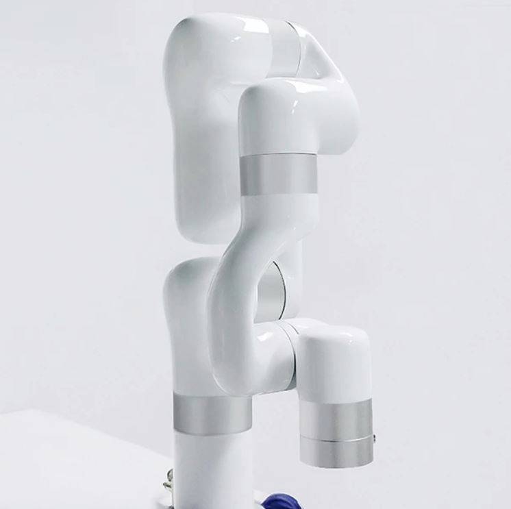 Moderní bílý robotický manipulátor s několika klouby, upevněný na stole. Rameno je v neutrální poloze.