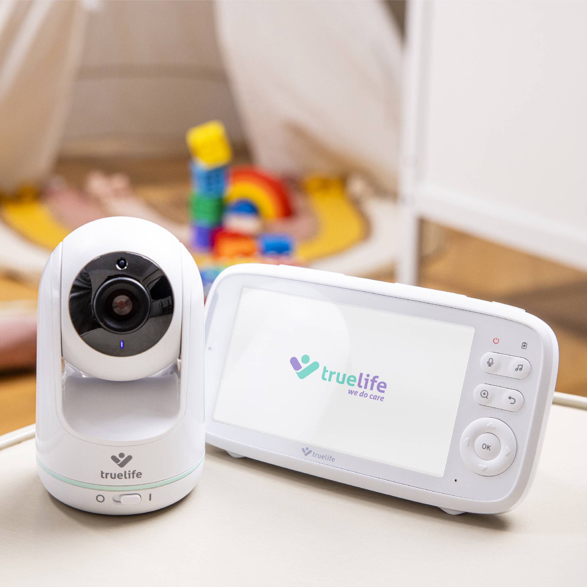 Elektronická chůvička s kamerou a monitorem ukazuje dítě, které si hraje na podlaze. Logo 'truelife - we do care' je viditelné.