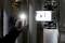 Jedna osoba drží svítící kapesní svítilnu vedle technologického zařízení s ventily a potrubím. Prostředí je slabě osvětlené.