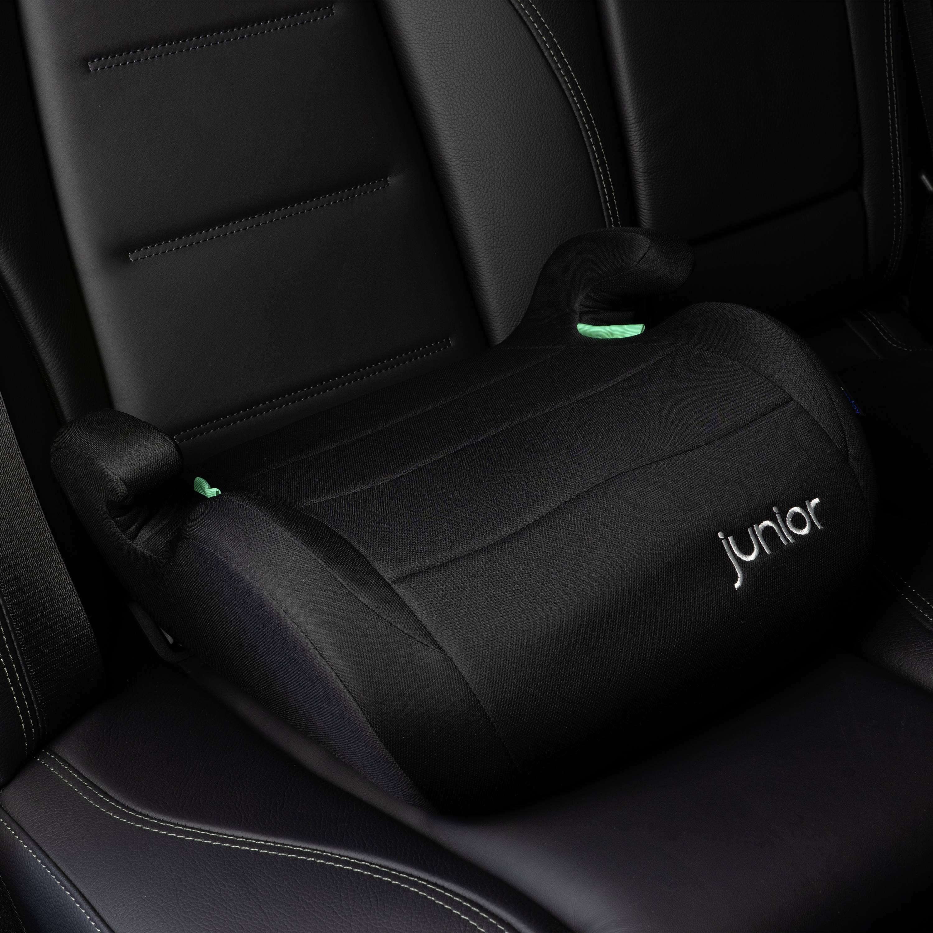 Černá dětská autosedačka se zeleným akcentem, umístěná na sedadle automobilu. Na boku je bílým písmem napsáno „Junior".