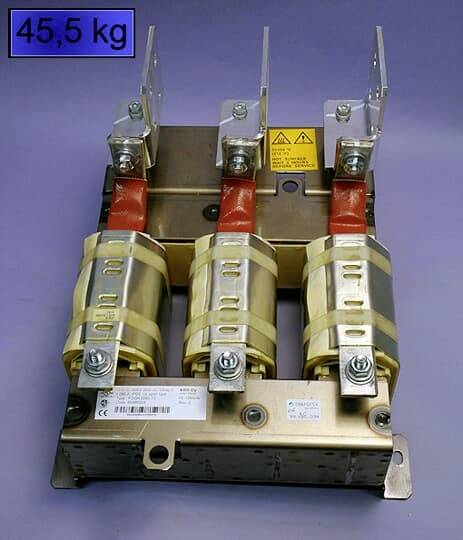 Elektrický výkonový vypínač se třemi červeno-zlatými přípojkami na kovovém podstavci. Vlevo nahoře je modře vyznačeno '45,5 kg'.