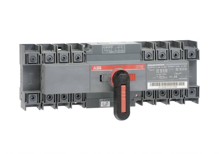 Elektrický přepínač zatížení s červenou pákou, obklopený několika svorkami. Jsou viditelné značení a informace o výrobci.
