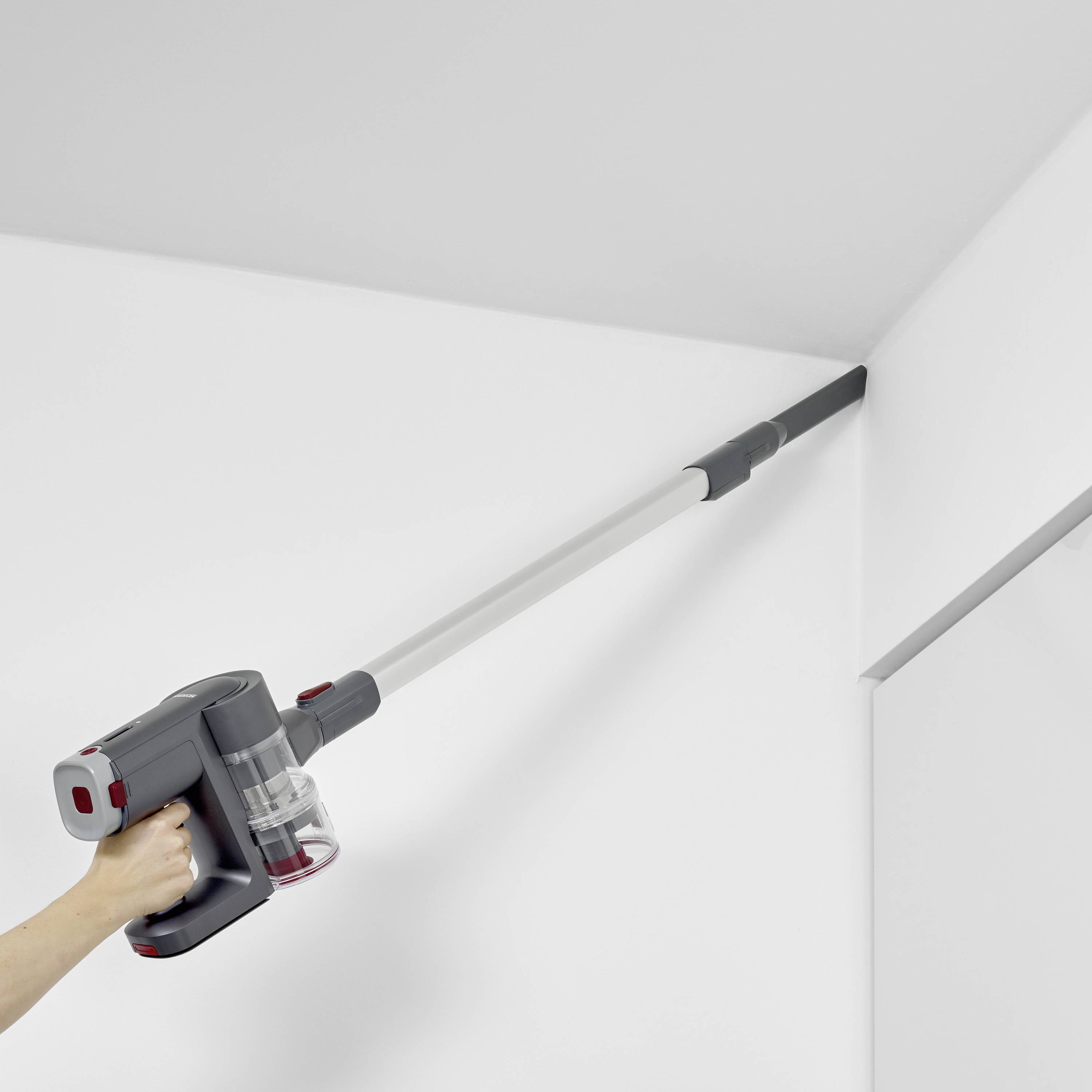 Vysavač s dlouhou trubicí odsává pavučinu v bílém rohu místnosti.