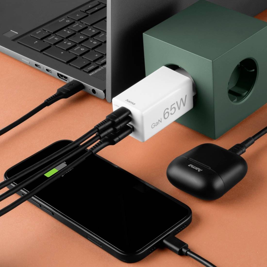 Smartphone a bezdrátová sluchátka jsou nabíjena pomocí 65W GaN nabíječe přes několik kabelů připojených do elektrické zásuvky.