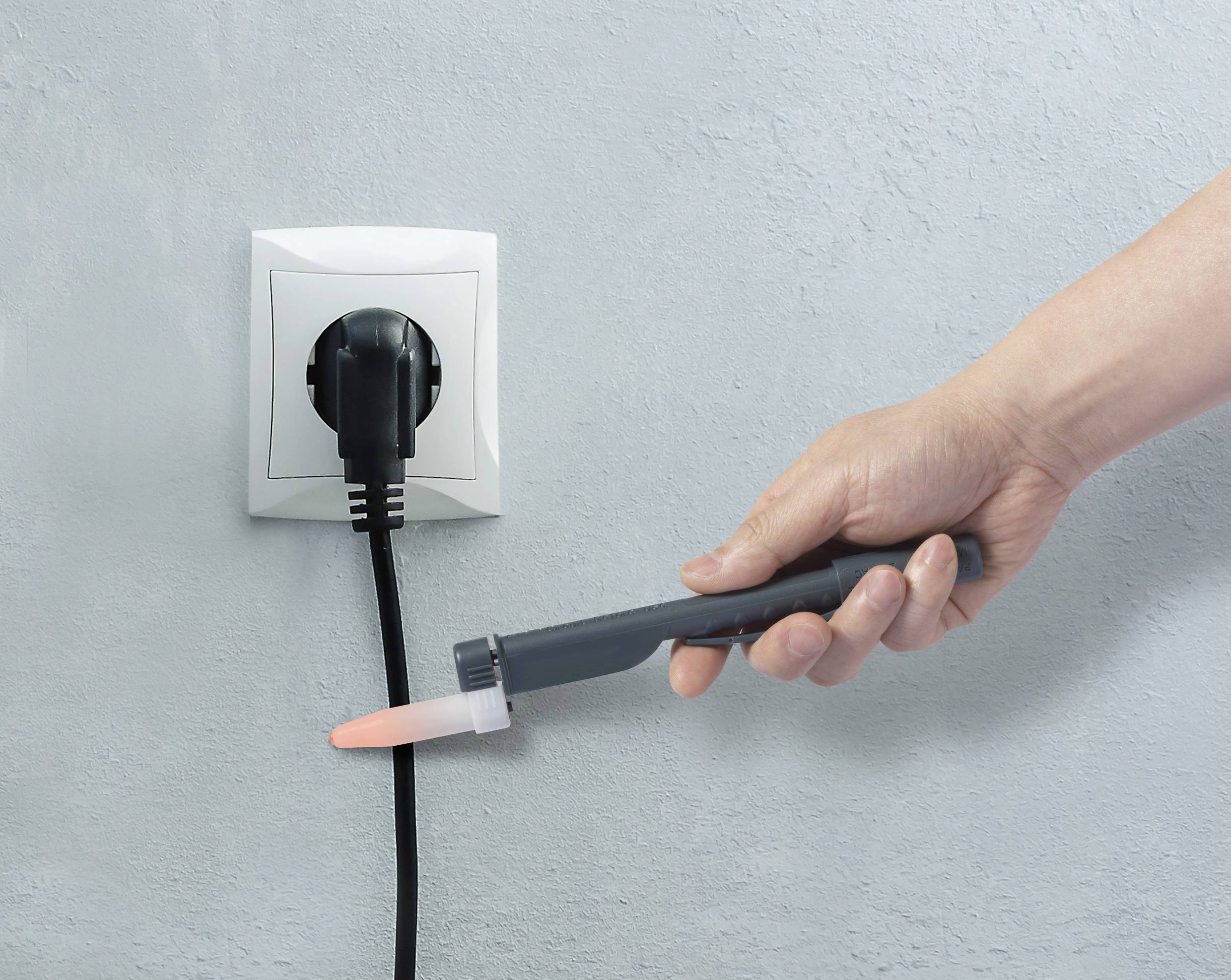Ruka testuje napětí na elektrickém zásuvce zkušebním přístrojem, do které je zapojen černý zástrčka.