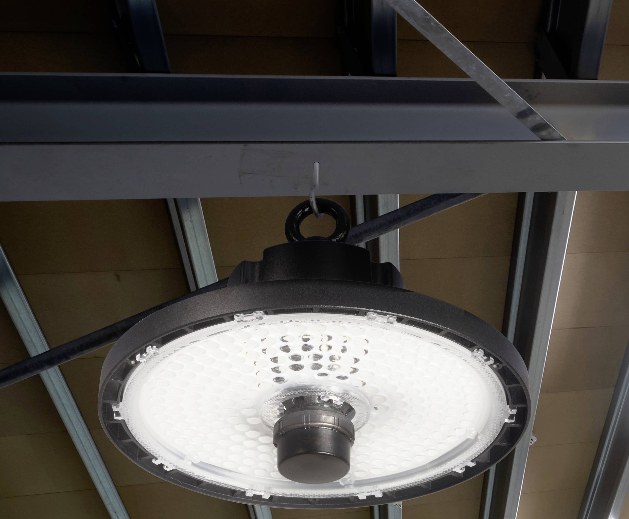 Kulatá LED lampa visí ze stropní kovové konstrukce. Lampa je zapnutá a svítí v industriálním prostředí.