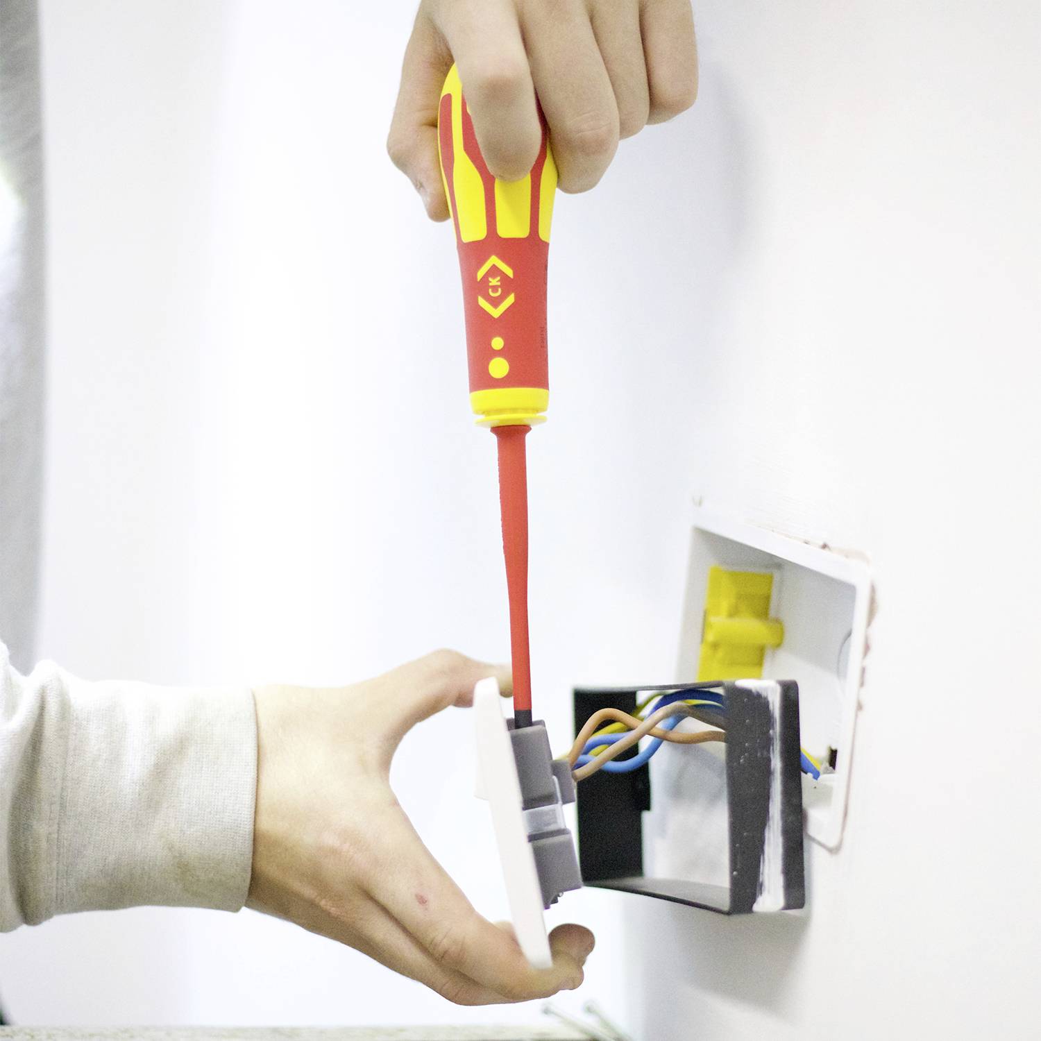 Osoba instaluje elektrickou zásuvku. Ruka drží šroubovák a propojuje barevné kabely se zásuvkou.