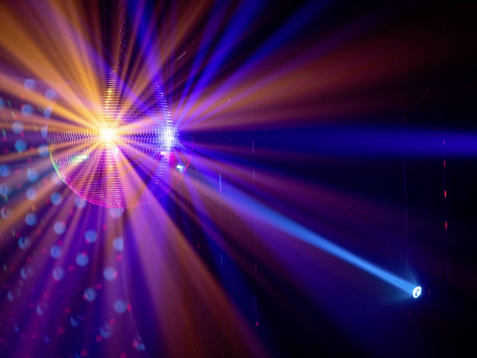 Diskotéková koule se otáčí a odráží barevné světlo v tmavé místnosti, čímž vytváří živoucí a slavnostní atmosféru.