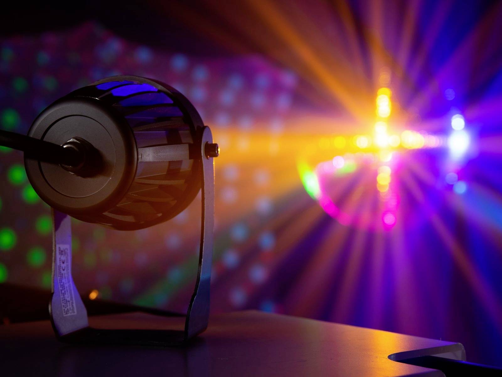 Jevištní osvětlení s barevnými paprsky svítícími v tmavém prostoru a reflektorem s černým rámováním v popředí.