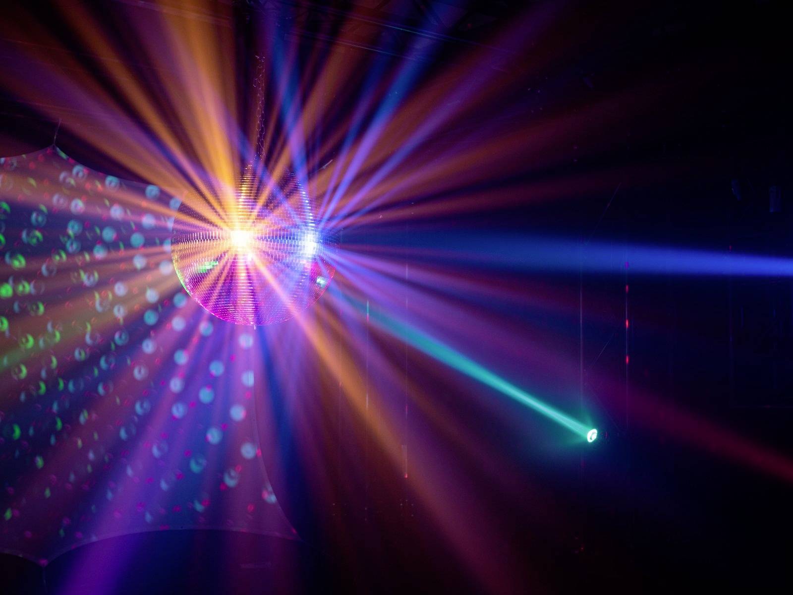 Barevné světelné paprsky a lasery promítají dynamické vzory v tmavé místnosti, podobně jako v atmosféře diskotéky.