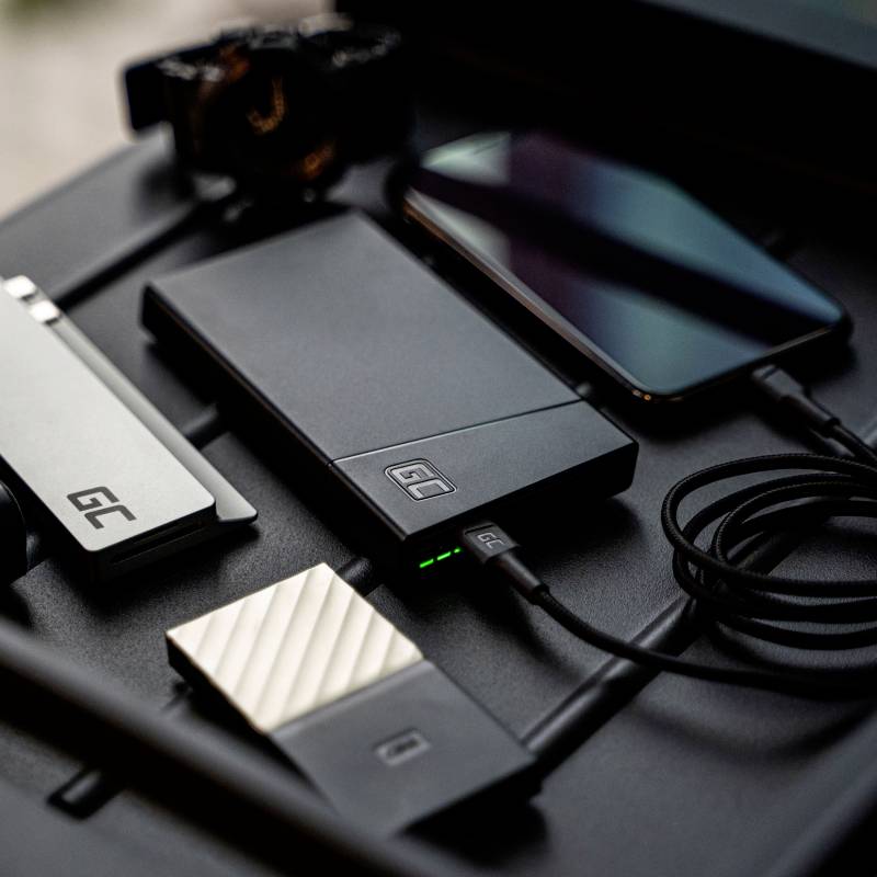 Několik elektronických zařízení a příslušenství na stole, včetně smartphonu, powerbabanky a externích paměťových modulů.