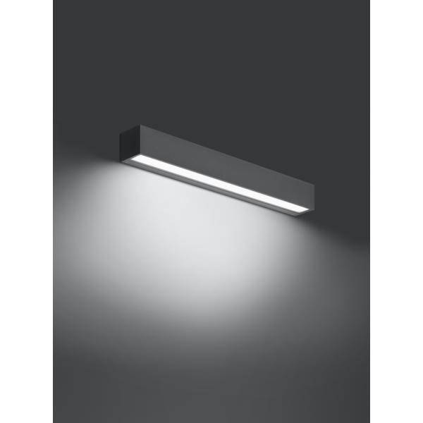 Nástěnná lampa s jednoduchým, moderním designem. Obdélníkový tvar, černá barva, vyzařuje měkké světlo směřující dolů.