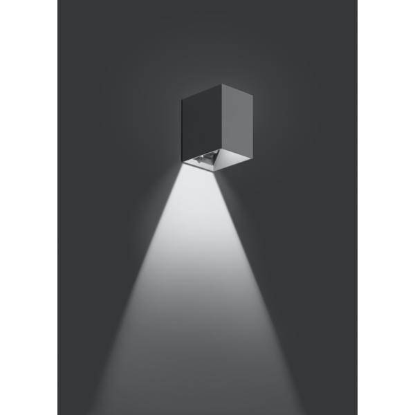 Nástěnná lampa s moderním, minimalistickým designem vrhá jasný světelný kužel na tmavém pozadí.