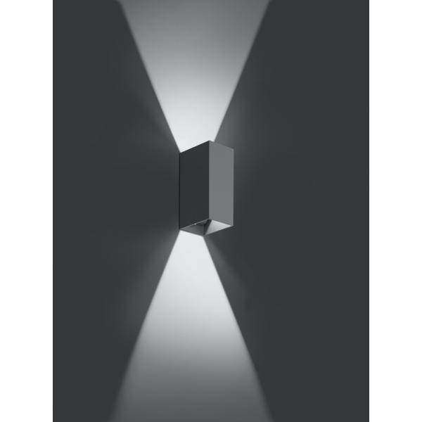 Moderní nástěnná lampa promítá světelné paprsky nahoru a dolů na šedou stěnu a vytváří stylový geometrický vzor.