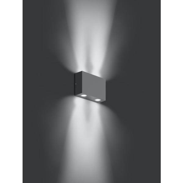 Kovová nástěnná lampa ve tvaru krychle, která vrhá světlo nahoru a dolů na tmavou stěnu a vytváří dekorativní vzor.